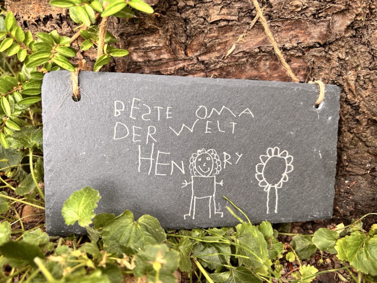 Schieferschild zum Aufhängen Kreidetafel mit der Aufschrift "Beste Oma der Welt" und einfachen Zeichnungen von Figuren.