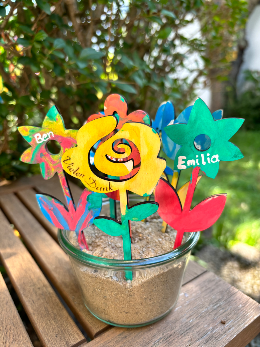 Kindergarten-Abschiedsgeschenk Bunte Papierblumen in einer Glasvase auf einem Holztisch im Garten.